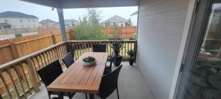 A cozy covered patio with a wooden dining table, black chairs, and potted plants, perfect for outdoor relaxation.