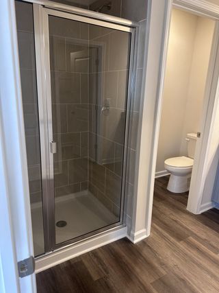 A modern bathroom with a sleek glass shower, neutral tiles, and rich wooden flooring.