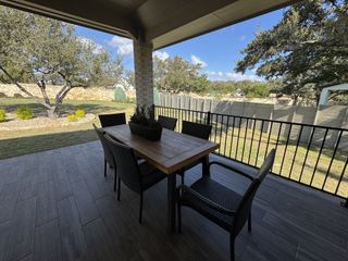 A cozy patio with wicker seating, a wooden table, and scenic views of a landscaped garden under a clear blue sky.
