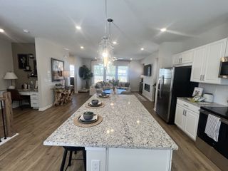 Model Home A spacious kitchen with a large granite island, white cabinetry, stainless steel appliances, and elegant pendant lighting.