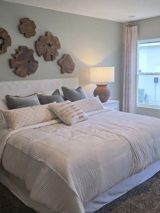 Model Home A cozy bedroom with textured bedding, decorative wood wall art, and a soft glow from a stylish lamp by the window.