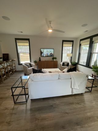 A cozy living room featuring plush seating, sleek wood flooring, large windows, and a modern ceiling fan for comfortable living.