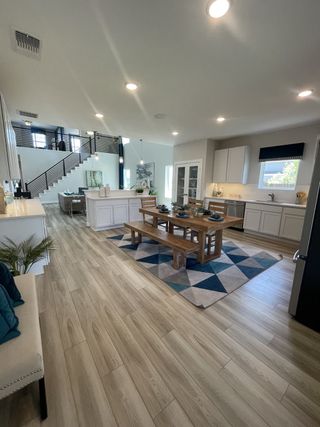 A spacious open-concept kitchen and dining area with light wood floors, modern cabinetry, and a rustic dining table.