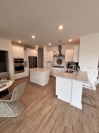 A spacious kitchen with white cabinets, wood-style flooring, and a large island with seating, perfect for entertaining.