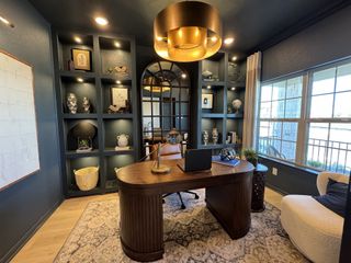 A sophisticated home office with dark blue built-ins, a wood desk, and a large window for ample natural light.