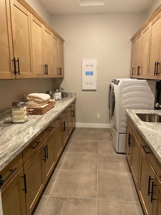 A spacious laundry room features light wood cabinets with black hardware, a gray granite countertop, and a white washer and dryer set.