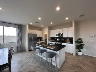 Model Home A modern kitchen with black countertops, white cabinets, a breakfast bar, and stylish lighting.
