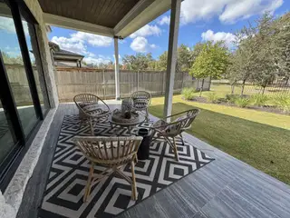 A relaxing backyard patio with woven wicker seating, a geometric outdoor rug, and a fence-lined view of lush greenery for peaceful outdoor living.