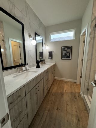 Model Home A modern bathroom featuring dual sinks, elegant wood cabinetry, and sleek fixtures under stylish lighting.