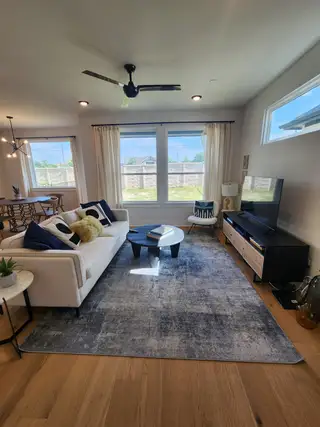 A cozy living room with a white sofa, large windows, modern ceiling fan, and stylish decor on a soft gray rug.