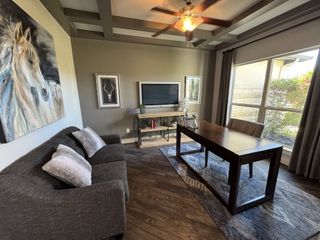 A cozy home office with a plush gray sofa, elegant artwork, large window, and modern wooden desk on a stylish rug.