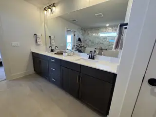 A modern bathroom featuring dual sinks on a dark wood vanity, elegant lighting, and a sleek, tiled shower area.