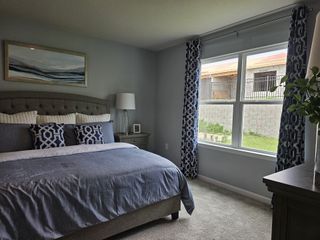 A cozy bedroom with soft grey tones, patterned curtains, plush beddings, and ample natural light through the window.
