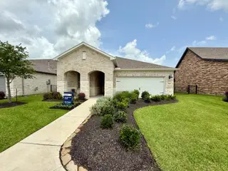 Street view A charming brick home with an arched entry and manicured lawn in Del Webb Fulshear by Del Webb (Fulshear, TX).