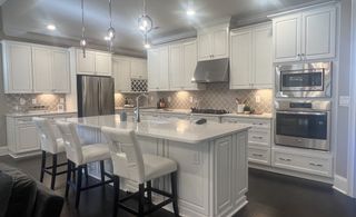 A modern kitchen with sleek white cabinetry, stainless steel appliances, and a large central island with elegant pendant lights.