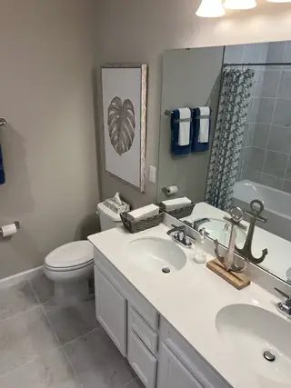 Model Home A chic bathroom featuring a double vanity, nautical decor, and elegant beige tiles.