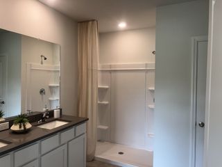 A clean, modern bathroom with dual sinks, a gray vanity, and a walk-in shower.