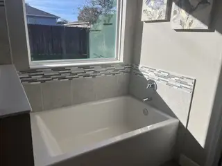 A bright bathroom with a deep soaking tub, chic mosaic tile accents, and large window views.