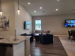 Model Home A modern living area with cozy seating, wall-mounted TV, and open dining, accented by stylish pendant lighting and wood floors.