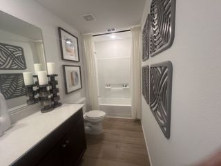 Model Home A modern bathroom with a sleek dark vanity, framed wall art, and a bathtub with white tile accents.