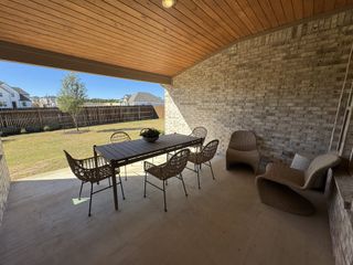 Model Home A cozy patio with wicker seating, a dining set, and a brick wall, overlooking a fenced backyard with a tree.