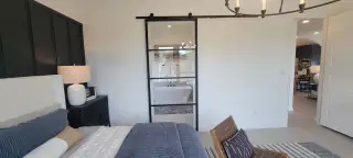 A cozy bedroom featuring a sliding glass door to a modern bathroom, stylish lighting, and elegant decor.