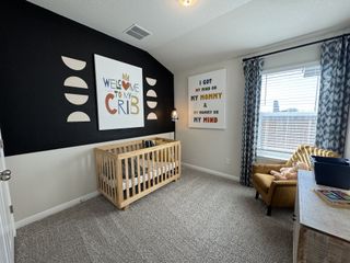 Model Home A cozy nursery featuring a wooden crib, bold wall art, and a comfy armchair by a window with patterned curtains.