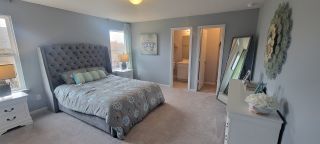 Model Home A bedroom with gray walls, an Ashley Furniture Sorinella Upholstered Platform Bed, white nightstands, a full-length mirror, and an open doorway to a bathroom.