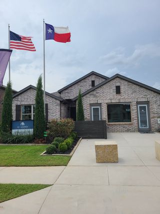 Model Home A charming brick home with manicured landscape and flags in Mobberly Farms by M/I Homes (Pilot Point, TX).
