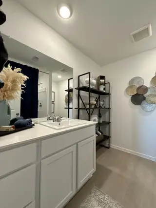 A sleek bathroom with white cabinetry, modern open shelving, and decorative wall accents.
