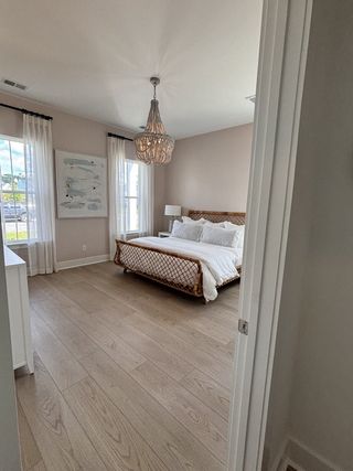 A serene bedroom with light wood flooring, a chic chandelier, and large windows allowing natural light.