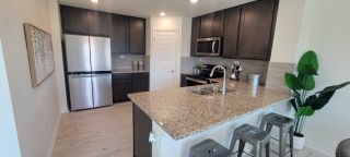 Model Home A modern kitchen in a Mission del Lago home, featuring dark wood cabinets, granite countertops, stainless steel appliances, and a kitchen island with bar stools (San Antonio, TX).
