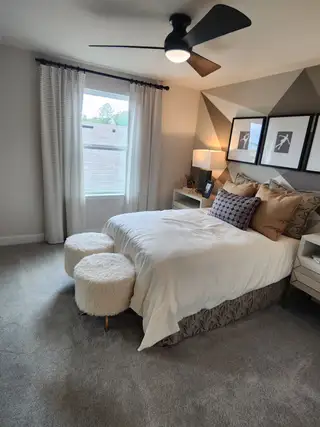 A cozy bedroom with geometric accent wall, plush bedding, chic lighting, and furry stools for a touch of elegance.