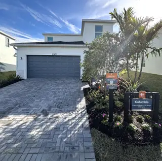 Street view A modern white home with a sleek gray garage and landscaped yard in Riverwood at Everlands: The Angler Collection by Lennar (Palm Bay, FL).