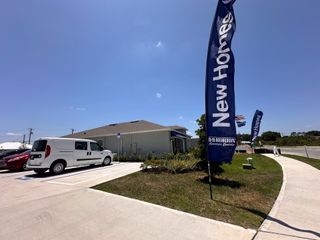 A welcoming entrance to Eagle Hammock by D.R. Horton (Eagle Lake, FL), featuring new home signs, lush landscaping, and blue skies.
