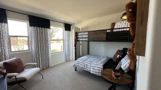 A cozy bedroom featuring a loft bed, playful décor, and ample natural light through large windows with patterned curtains.
