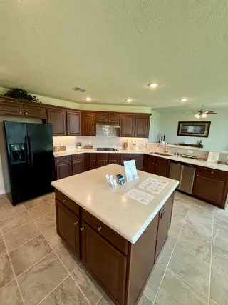 A spacious kitchen with dark wood cabinets, light countertops, and modern appliances on a tiled floor.