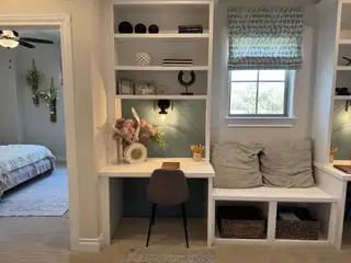 Cozy study nook with built-in shelves, chic chair, and soft lighting, adjacent to a tranquil bedroom space.