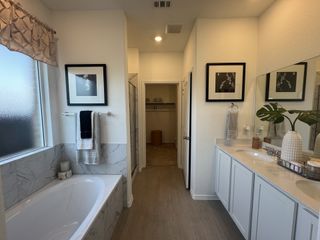 A bright bathroom featuring a marble-tiled bathtub, dual sinks, elegant decor, and a spacious feel.