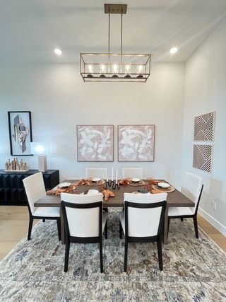A chic dining room with elegant lighting, abstract art, and a sleek wooden table set for six on a patterned rug.