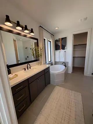 Model Home A stylish bathroom with a dark vanity, gold hardware, and a soaking tub in Esperanza by Perry Homes (Boerne, TX).
