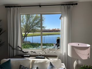 Model Home A cozy living room with a large window offering serene lake views, accented by soft drapes and a stylish lamp.