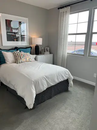 A cozy bedroom with neutral walls, stylish artwork, soft bedding, and large windows for natural light.