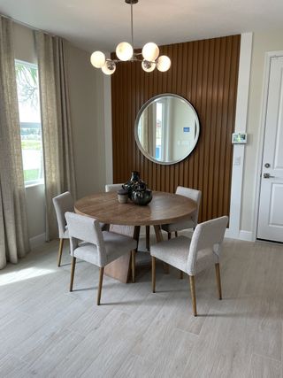 A chic dining area with a round wood table, modern chandelier, and textured accent wall featuring a round mirror.