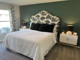 Model Home A cozy bedroom featuring a patterned headboard, white bedding, and elegant bedside lamps, complemented by a dark accent wall.