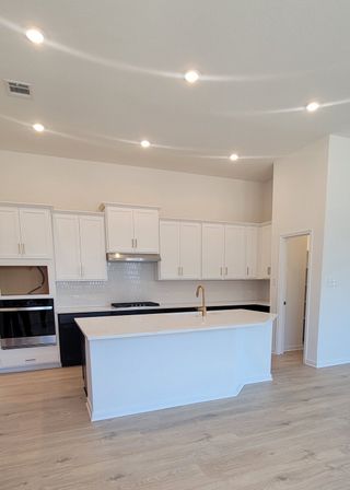 A bright, open kitchen with white cabinetry, a center island, and wood-look flooring, in a Davis Ranch home by Coventry Homes (San Antonio, TX).