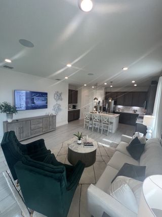 Model Home A modern open-concept living area with chic green chairs, a cozy sofa, and a sleek kitchen featuring a center island.