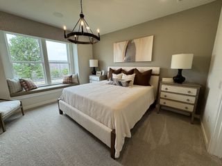 Model Home A cozy bedroom with a neutral palette, featuring a large window seat and modern chandelier.