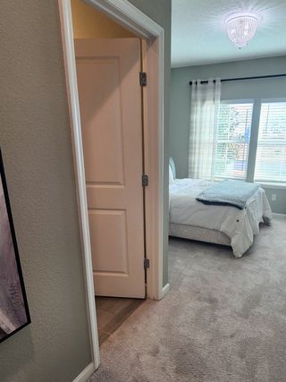 Model Home A cozy bedroom with soft carpeting, a stylish chandelier, and natural light through large windows with sheer curtains.