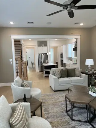 An inviting living area with cozy seating, a ceiling fan, and an open view into a modern kitchen with sleek appliances.